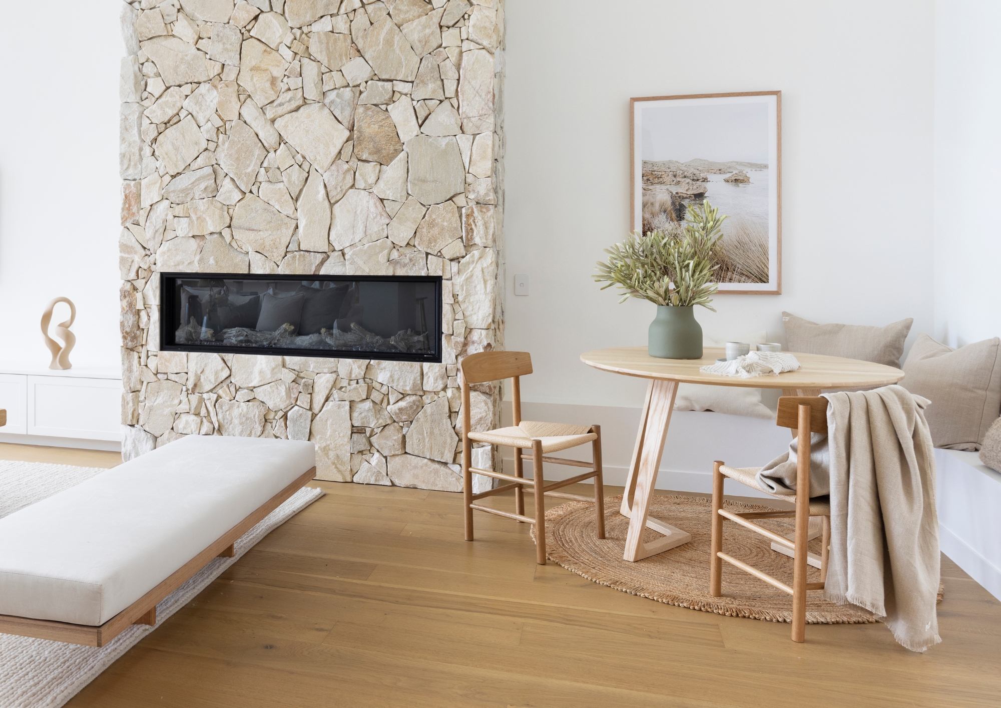 Aspirational round timber Kantet Dining Table in a modern living space with stone fireplace and Scandi seating.