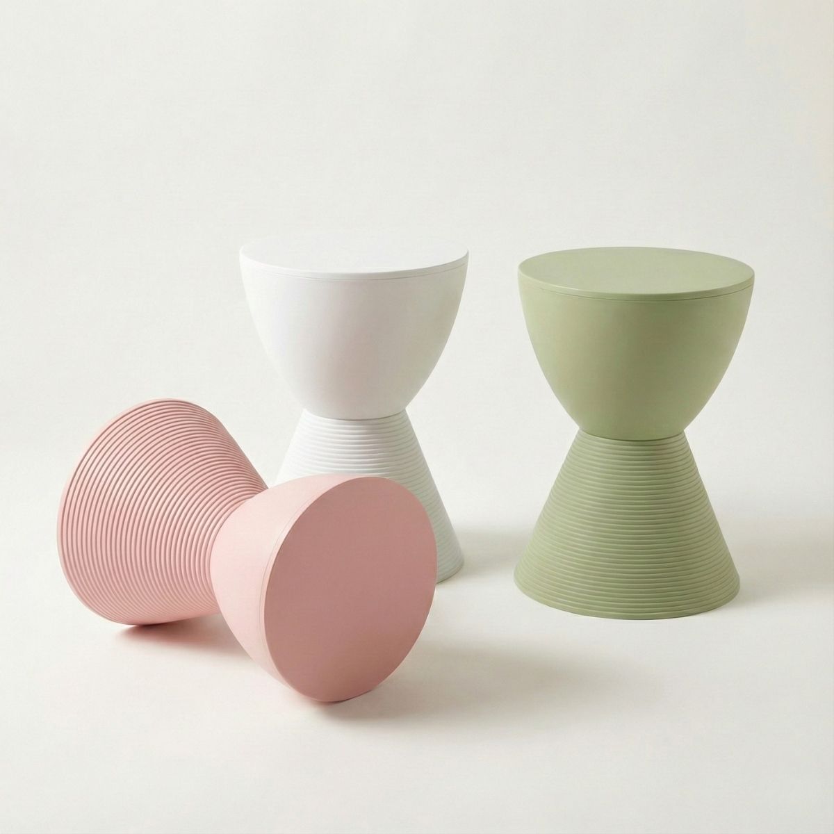 Group of three Replica Prince AHA Stools in white, pink, and green, showcasing their geometric hourglass shape and versatility as outdoor side tables.