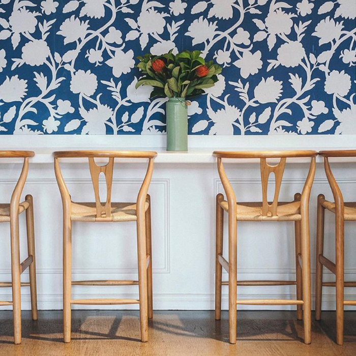Four Replica Wishbone stools with solid Ash frame and natural cord seats, styled in a caf&eacute; at a white bar table.