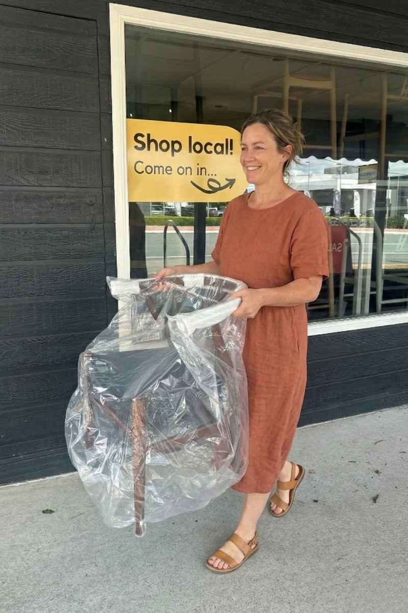 Happy customer leaving the Replica Furniture Kedron showroom with a new dining chair, demonstrating our immediate pick-up service.