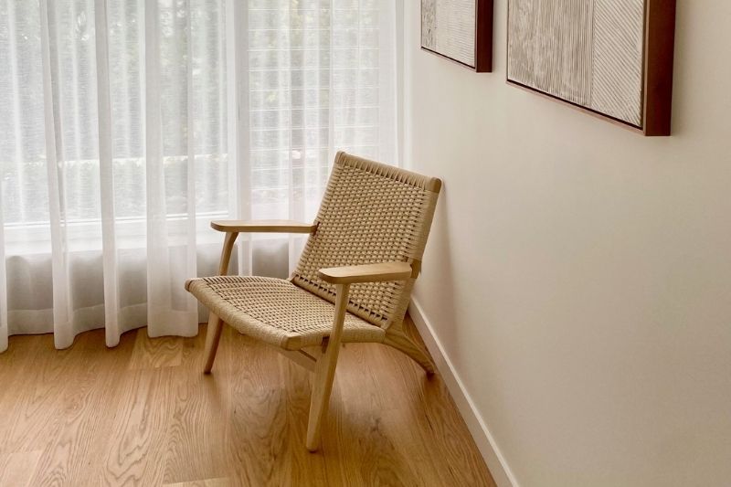 Replica Hans Wegner CH25 Easy Chair featuring a woven seat, styled in a low-profile Japandi living room.