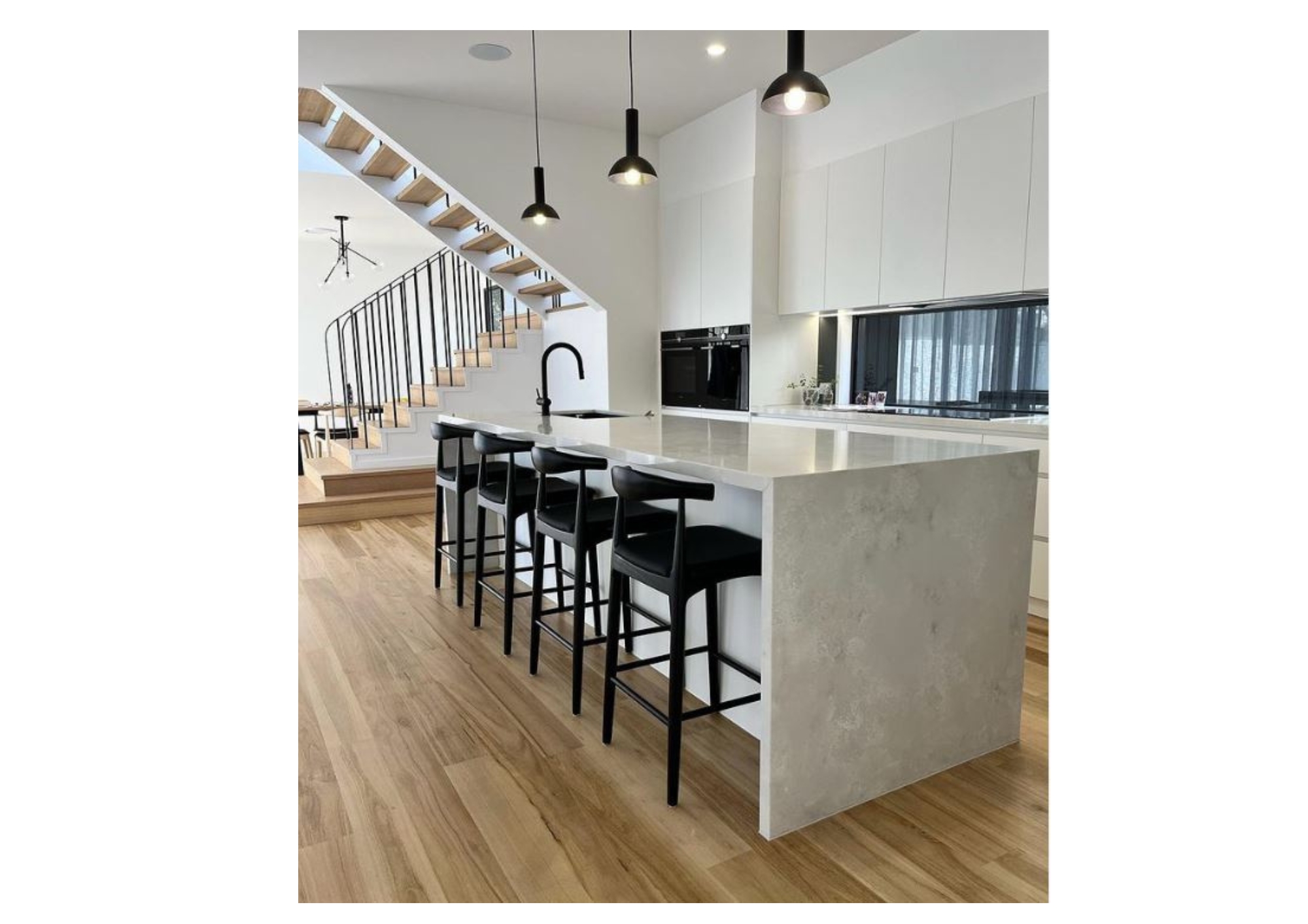 Modern kitchen island with black upholstered Replica Hans Wegner Elbow stools and black pendant lights.