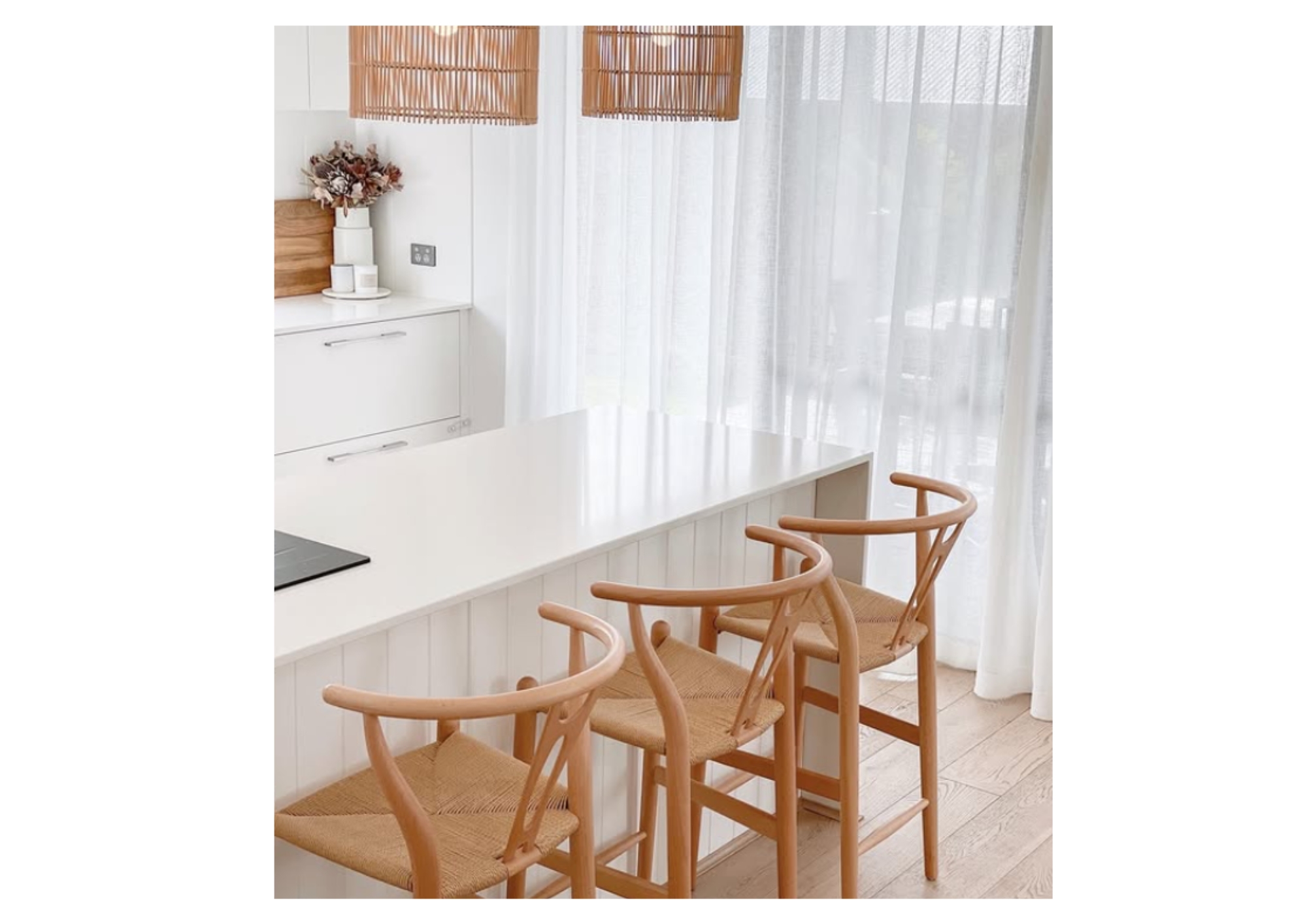 Coastal kitchen counter with three natural timber Wishbone stools and woven pendant lights.